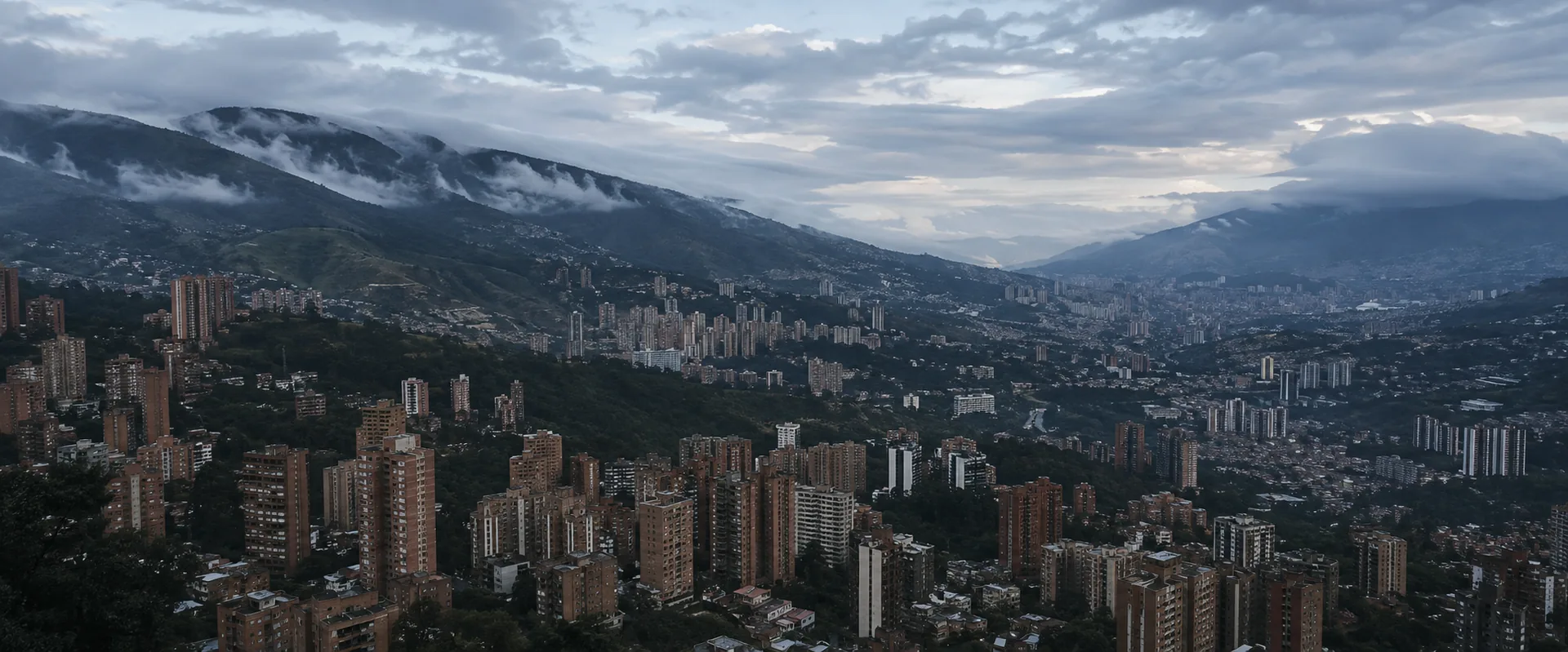 Medellín seen from the eastern hillside at dawn, brick apartment towers filling the valley floor with cloud sitting along the Andean ridgelines.